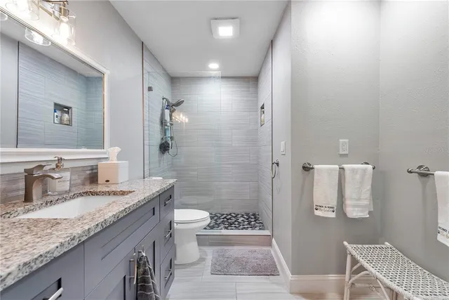 a bathroom with a granite countertop sink a toilet a mirror and shower