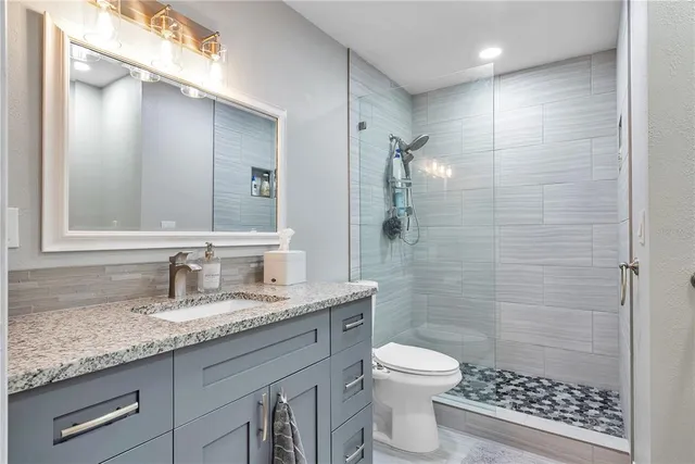 a bathroom with a granite countertop sink a toilet a mirror and shower