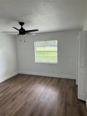 an empty room with wooden floor ceiling fan and windows