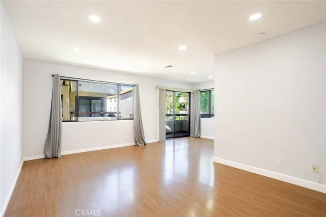 a view of an empty room with wooden floor and a kitchen