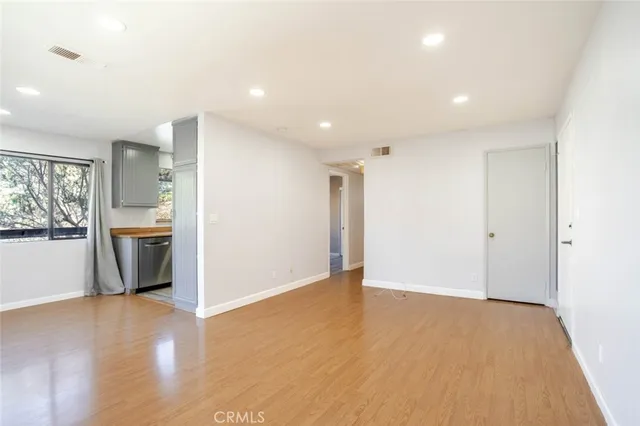 a view of an empty room with wooden floor and a kitchen