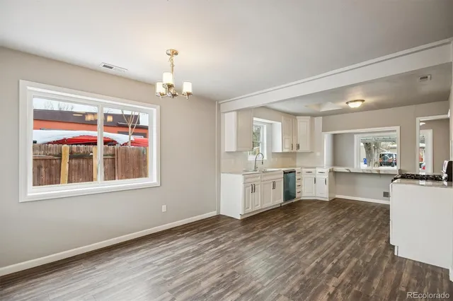 a large white kitchen with granite countertop a stove top oven a sink dishwasher and white cabinets with wooden floor