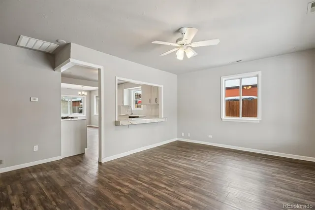 an empty room with wooden floor chandelier fan and windows