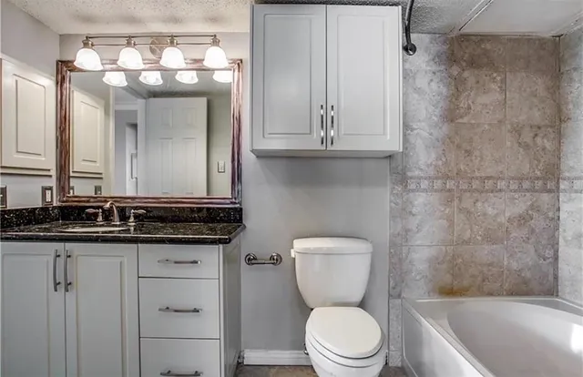 a bathroom with a granite countertop sink a toilet a mirror and bathtub