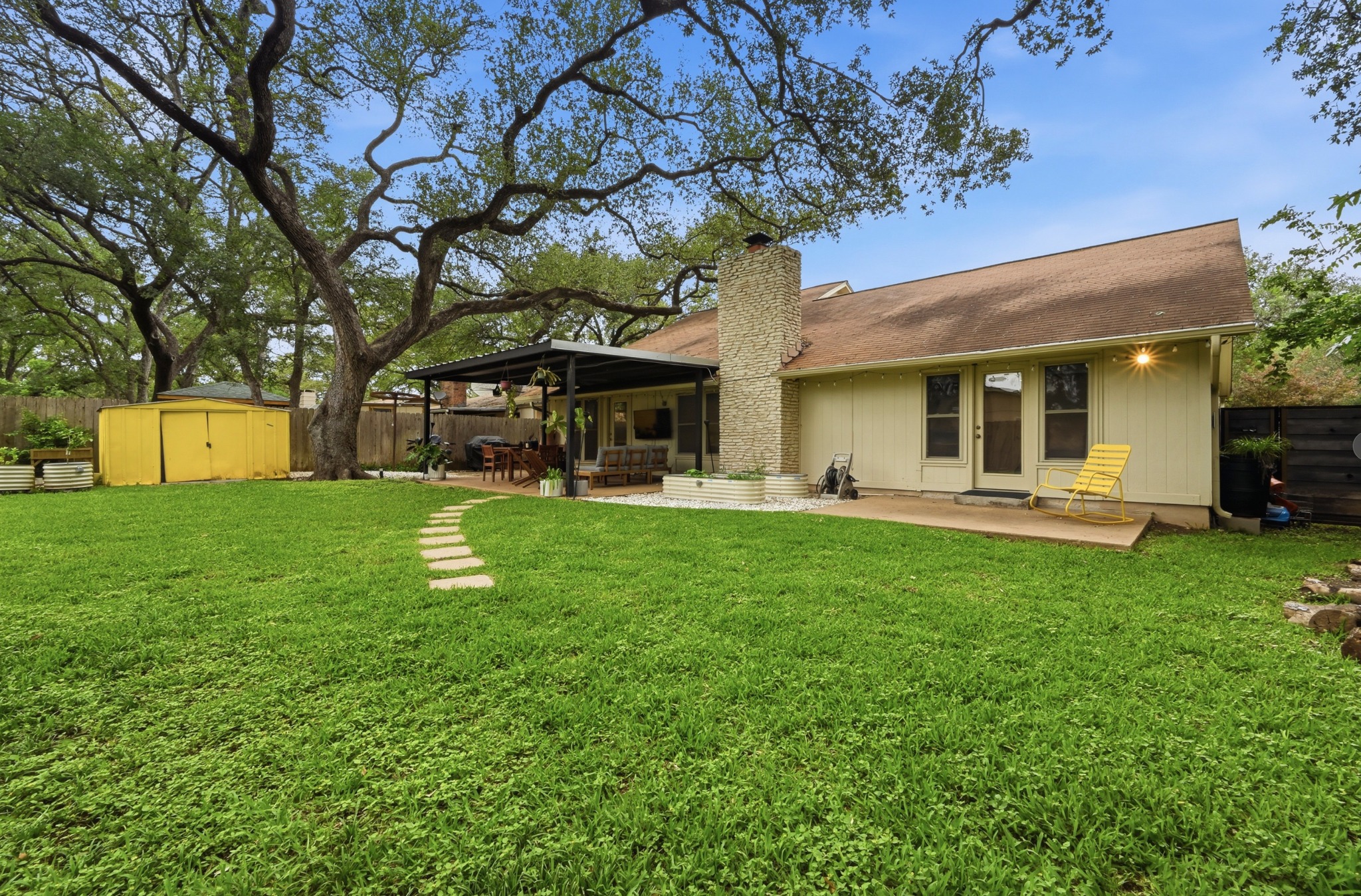 2509 Redleaf Lane Austin, TX 78745 - Photo 23 of 28 Expansive backyard featuring a mature central tree, a stone paver pathway, and a covered patio area with a dark metal roof
