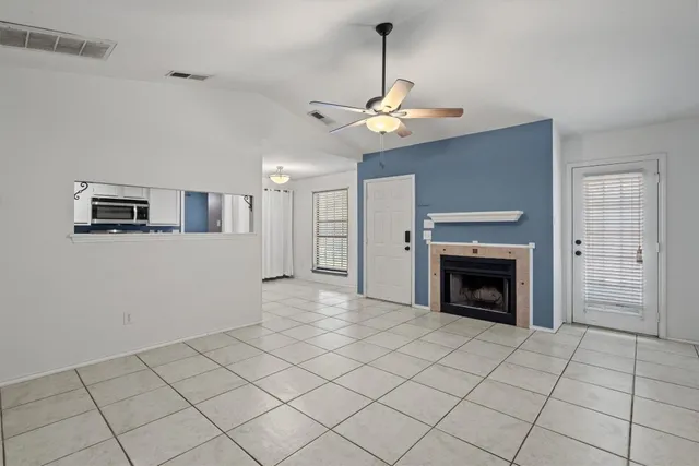 a view of a livingroom with a fireplace a ceiling fan and windows