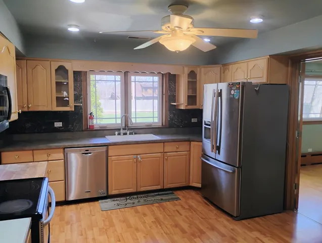 a kitchen with stainless steel appliances granite countertop a refrigerator a sink dishwasher a stove and a dining table with wooden floor