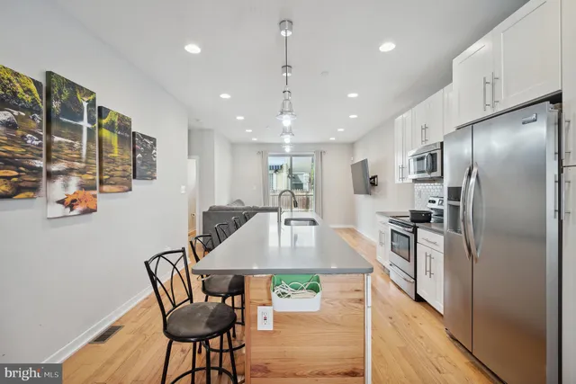 a kitchen with stainless steel appliances granite countertop a refrigerator a stove a sink a dining table and chairs with wooden floor