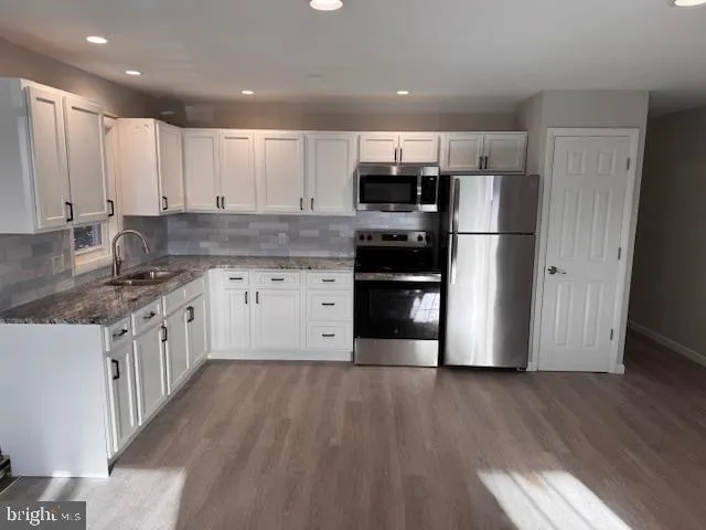 a kitchen with stainless steel appliances granite countertop a refrigerator a stove top oven a sink and dishwasher with wooden floor