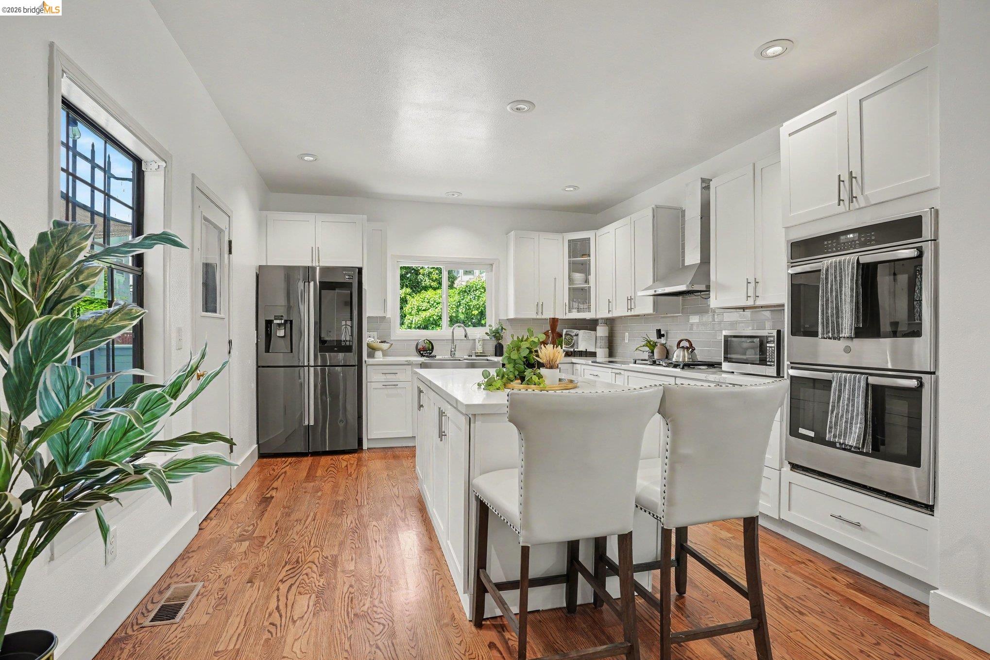 1433 Myrtle Street Oakland, CA 94607 - Photo 5 of 25 Open-concept kitchen featuring an oversized island with seating, white shaker cabinetry, stainless steel appliances, and wood-finish flooring