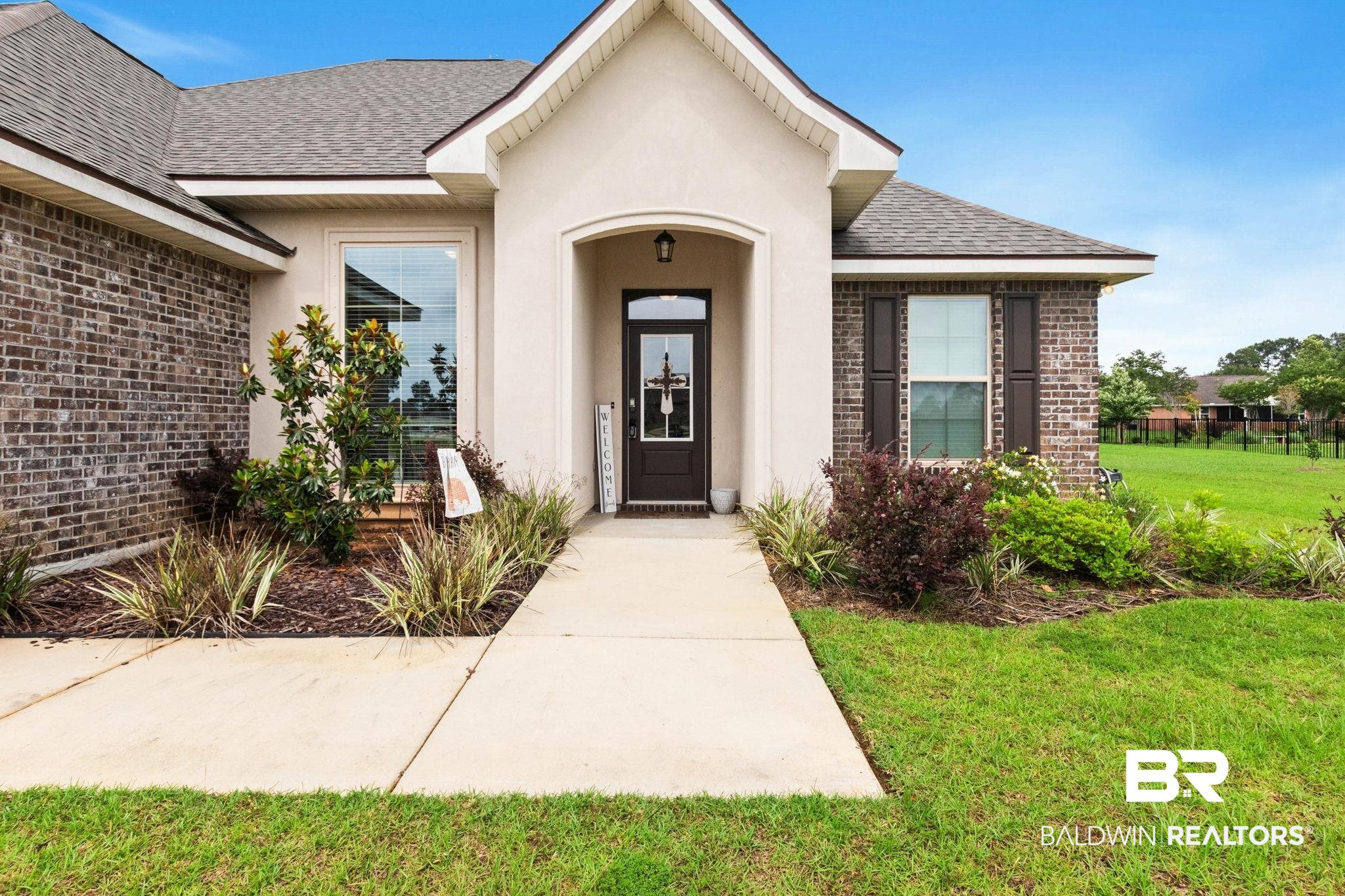22244 Hibiscus Circle Foley, AL 36535 - Photo 2 of 51 Brick and stucco exterior featuring a dark paneled front door, an arched entryway, established landscaping, a concrete walkway, and a manicured lawn