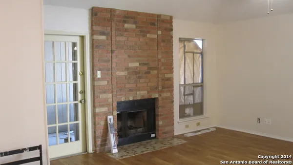a view of an empty room with wooden floor and a fireplace