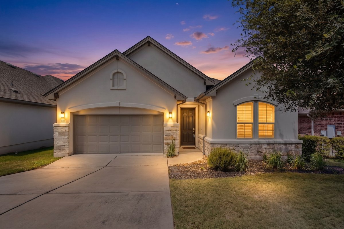 2617 Milan Meadows Drive Leander, TX 78641 - Photo 39 of 40 Illuminated entryway with an attached garage and stone accents welcomes you home under a twilight sky.