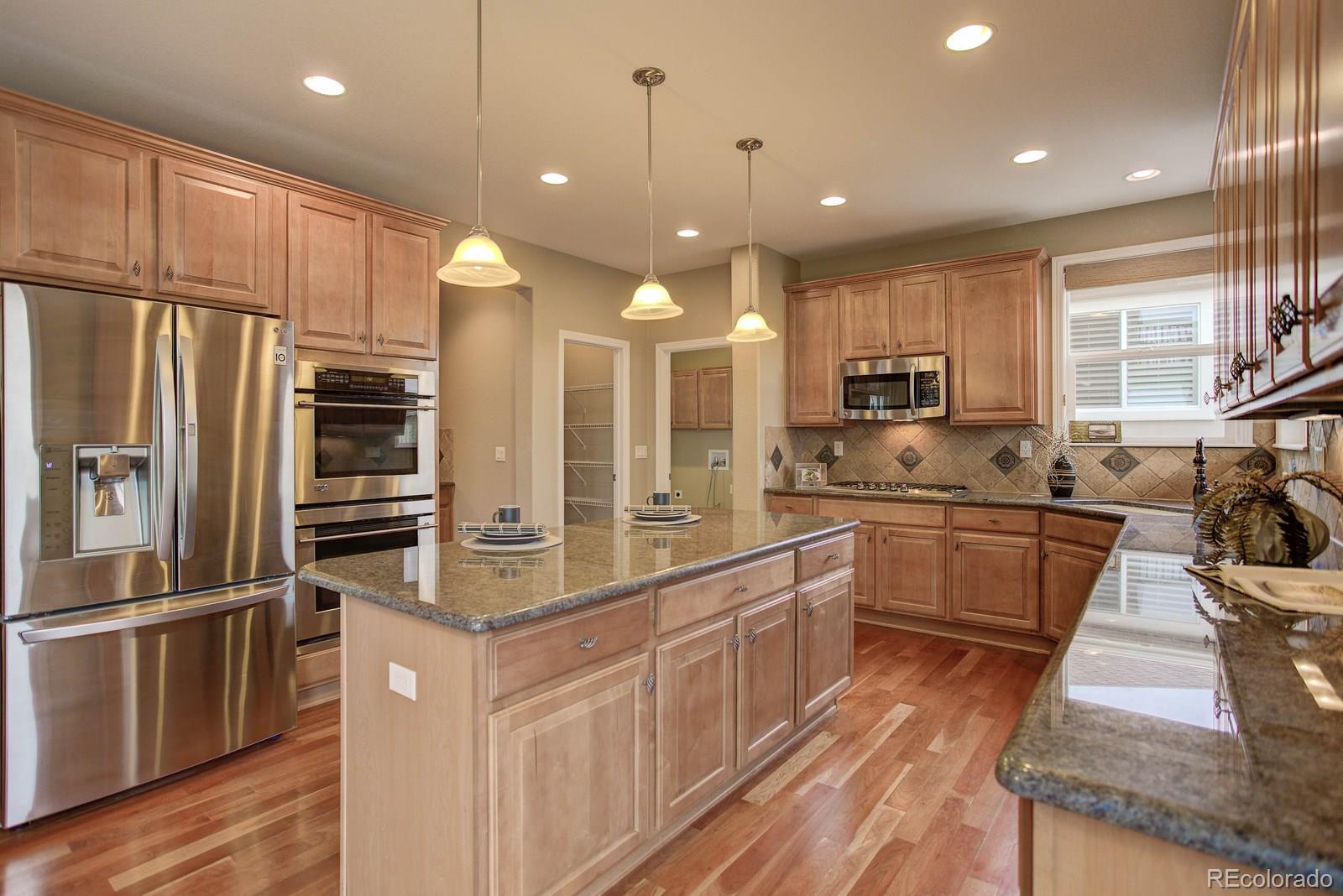 10879 Glengate Circle Highlands Ranch, CO 80130 - Photo 13 of 35 a kitchen with stainless steel appliances granite countertop a refrigerator a sink dishwasher a oven and a dining table with wooden floor