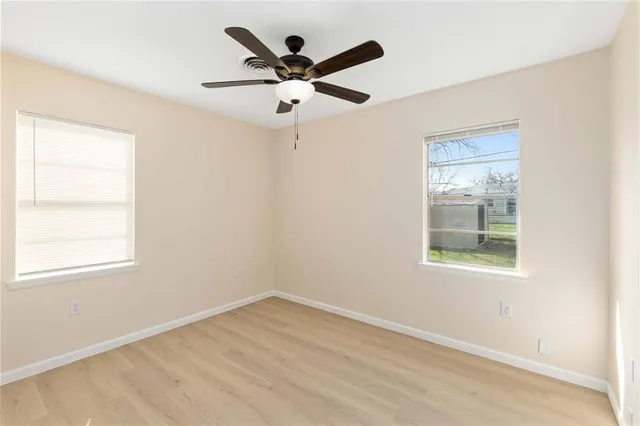 an empty room with wooden floor ceiling fan and windows