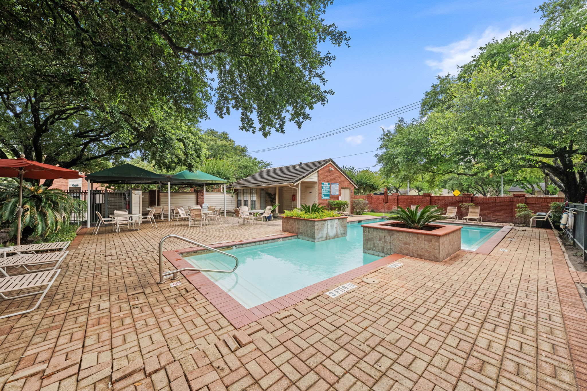 2211 South Kirkwood Road, Unit 1 Houston, TX 77077 - Photo 15 of 16 The wider view of the pool area reveals the full scope of the amenity — a full brick paver surround with room to spread out, covered seating with shade umbrellas, and a mature oak canopy overhead that gives the entire space an established, private quality the photos don't fully capture at closer range.