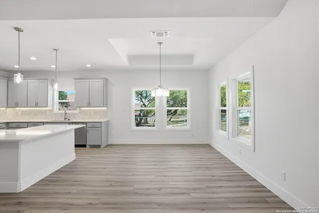 a large kitchen with kitchen island granite countertop a stove a sink dishwasher and white cabinets with wooden floor