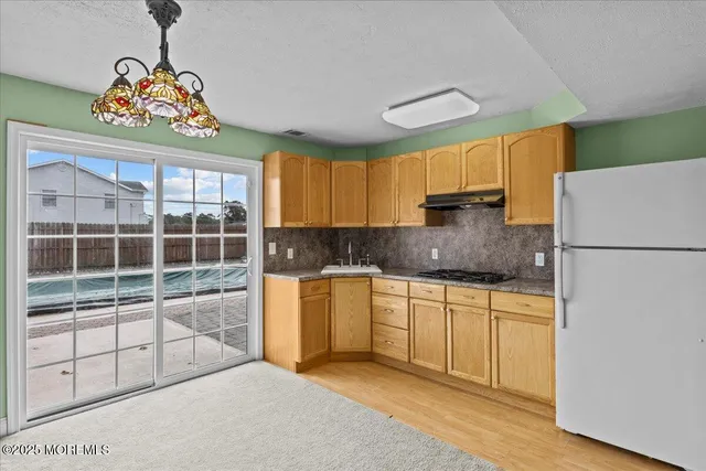 a kitchen with a refrigerator a sink dishwasher a stove a dining table and chair with wooden floor