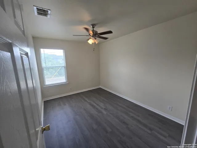 an empty room with wooden floor fan and windows