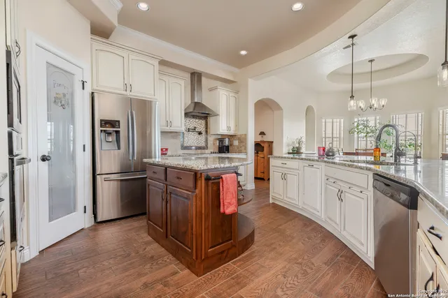 a kitchen with stainless steel appliances granite countertop a refrigerator a sink dishwasher a stove and white cabinets with wooden floor