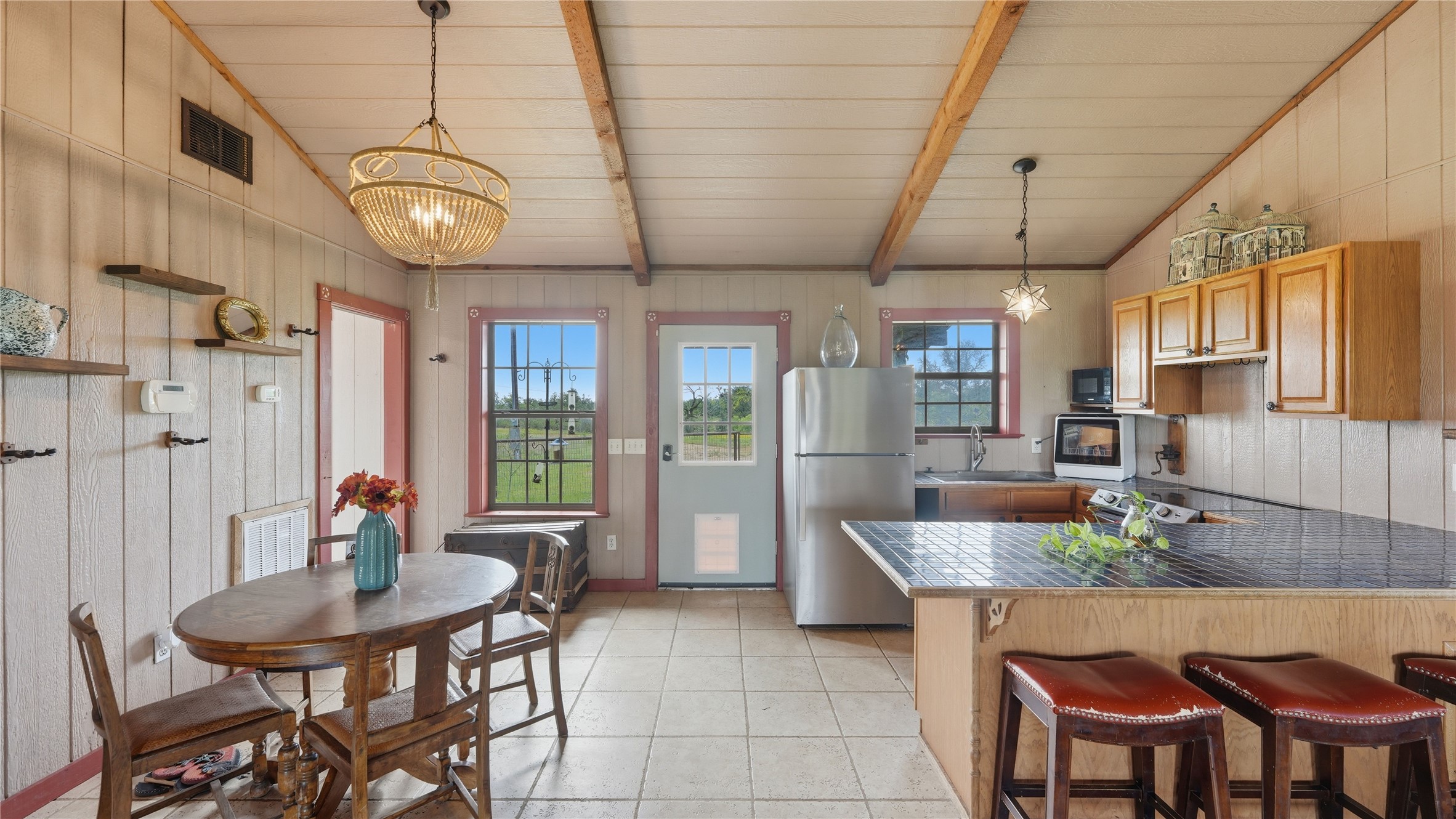 127 Offer Llano, TX 78643 - Photo 39 of 40 Kitchen and dining area featuring a tile floor, exposed ceiling beams, wood-paneled walls, and a kitchen island with seating