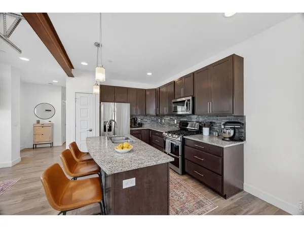 a living room with stainless steel appliances kitchen island granite countertop a refrigerator a stove a sink dishwasher and a stove with wooden floor