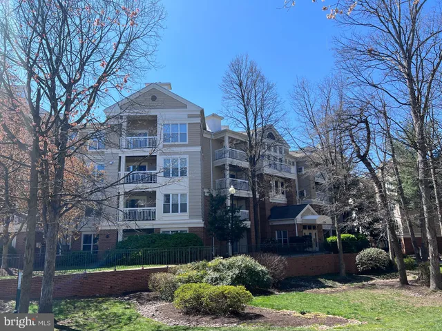 a front view of a residential apartment building with a yard and large trees
