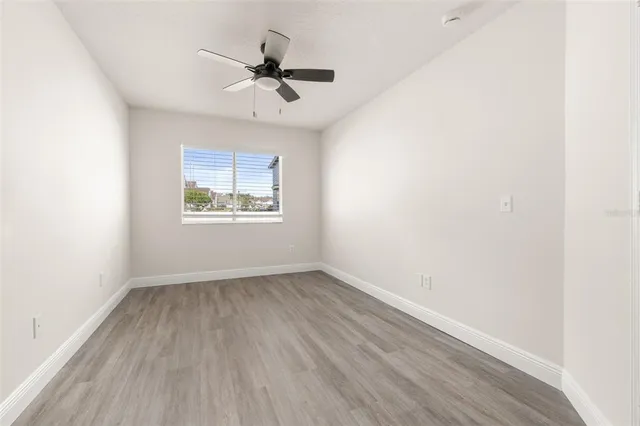 an empty room with wooden floor chandelier fan and windows