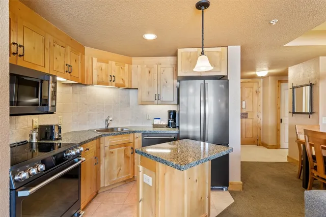 a kitchen with stainless steel appliances granite countertop a sink a stove a refrigerator cabinets and a dining table with wooden floor