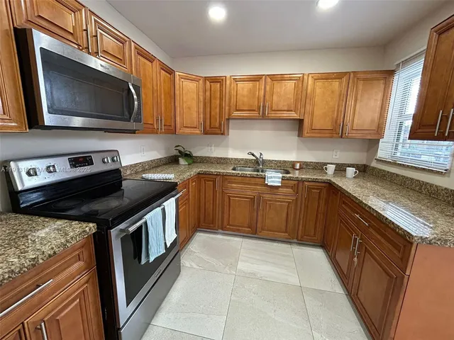 a kitchen with granite countertop stainless steel appliances a sink window and cabinets