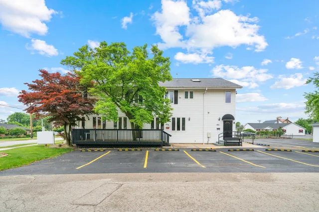 a view of a white house with a big yard plants and large trees
