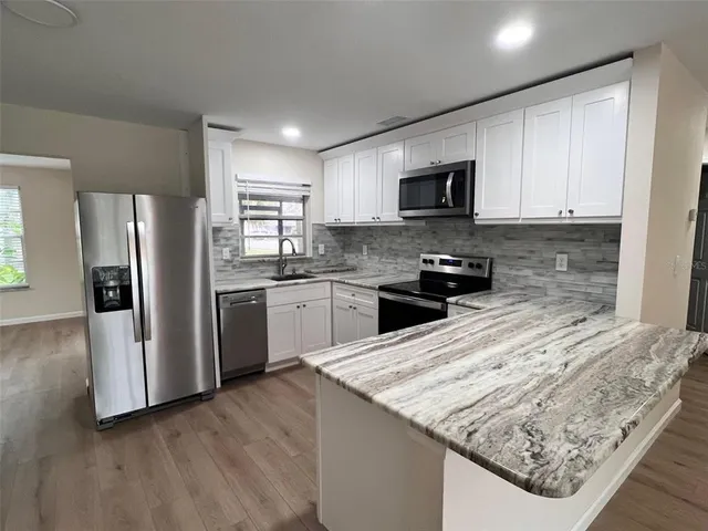 a kitchen with granite countertop a refrigerator a sink dishwasher a stove and white cabinets with wooden floor