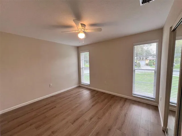 an empty room with wooden floor fan and windows