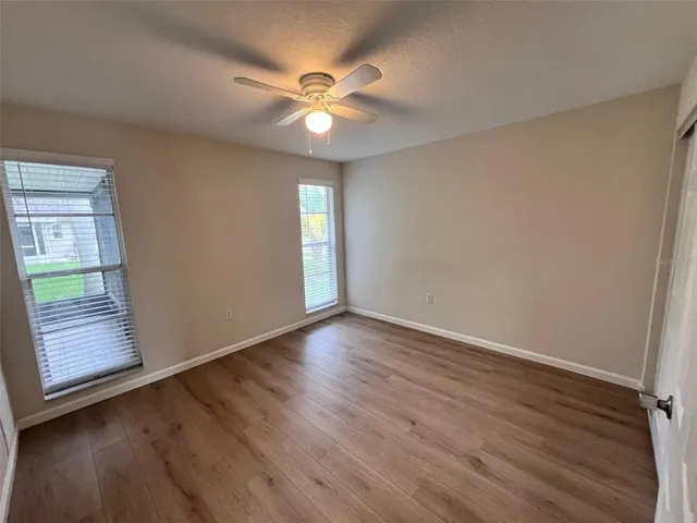 an empty room with wooden floor fan and windows