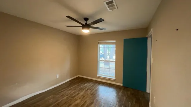 an empty room with wooden floor fan and windows