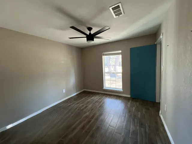 an empty room with wooden floor fan and windows