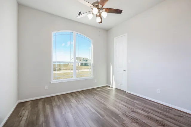 an empty room with wooden floor chandelier fan and windows