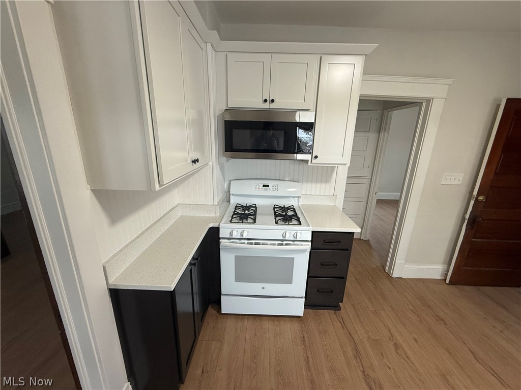 3612 Riverside Avenue Cleveland, OH 44109 - Photo 7 of 22 Kitchen featuring white upper cabinetry, dark lower cabinetry, light-toned countertops, a white gas range, and a stainless steel microwave
