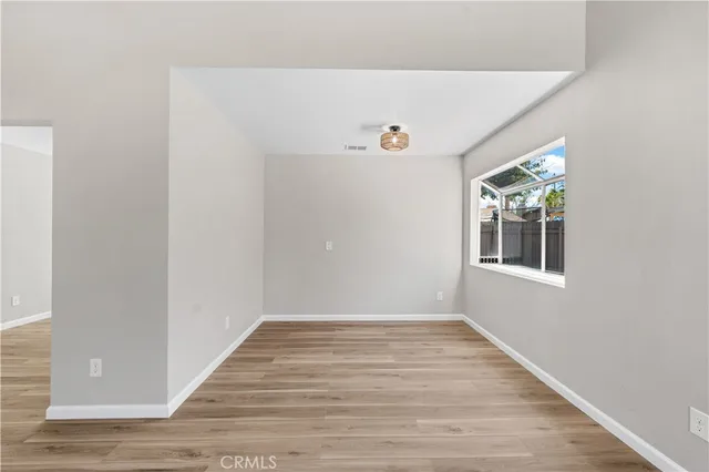 a view of an empty room with wooden floor and window