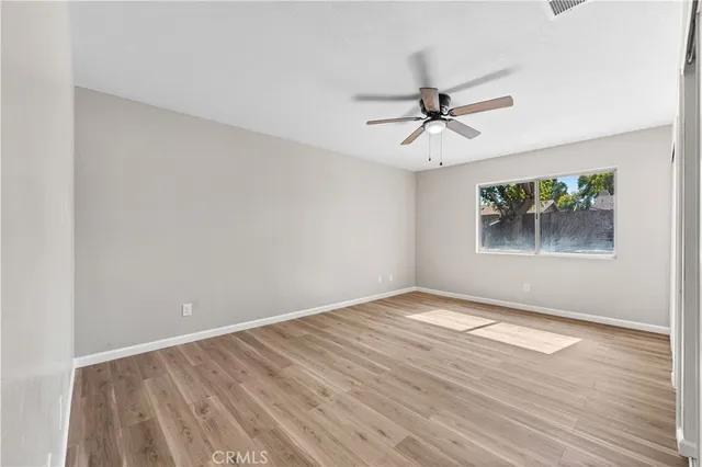 an empty room with wooden floor ceiling fan and windows