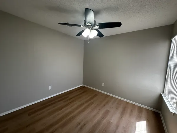 an empty room with wooden floor fan and windows