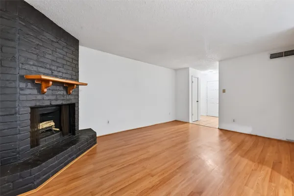 a view of an empty room with wooden floor fireplace and a window
