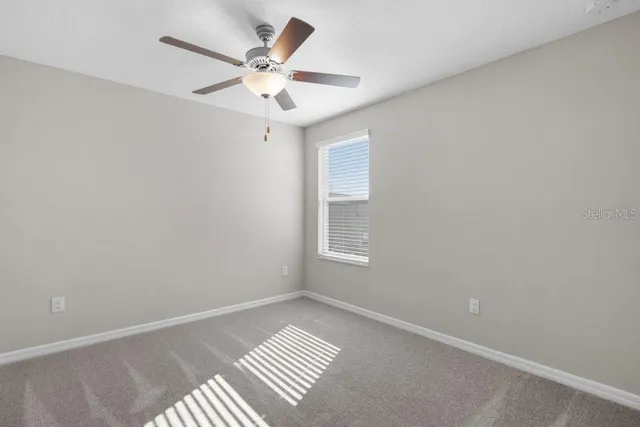 an empty room with a chandelier fan and windows