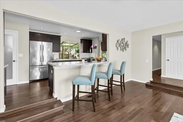 a kitchen with stainless steel appliances granite countertop a dining table chairs refrigerator and sink