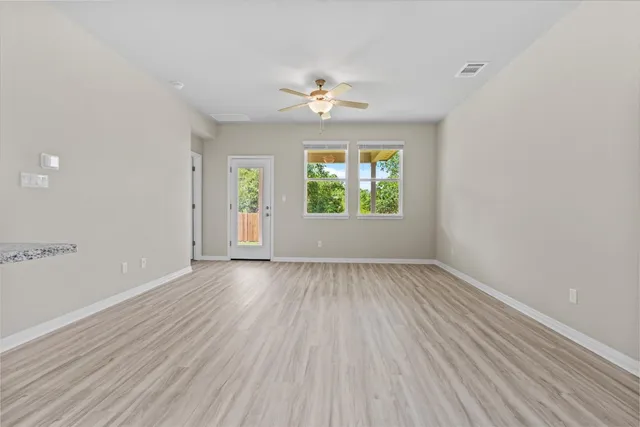 an empty room with wooden floor chandelier fan and windows
