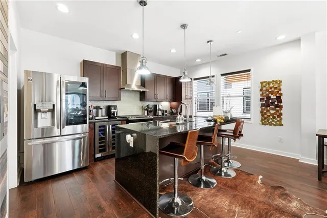 a kitchen with stainless steel appliances kitchen island granite countertop a refrigerator a stove a sink a dining table and chairs with wooden floor