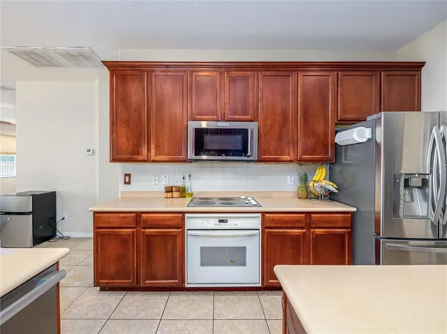 a kitchen with stainless steel appliances granite countertop a stove top oven a refrigerator and a sink with wooden cabinets