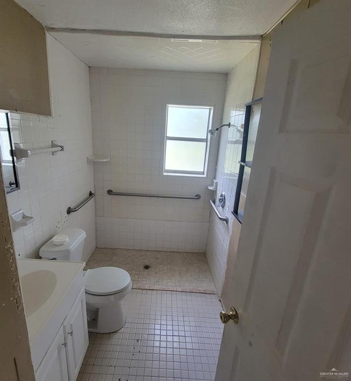 3135 Southmost Road Brownsville, TX 78521 - Photo 4 of 9 Full bathroom featuring tile walls, a shower stall, toilet, tile patterned flooring, and vanity