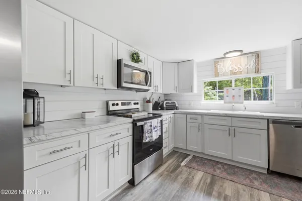 a kitchen with granite countertop white cabinets white appliances a sink and a window