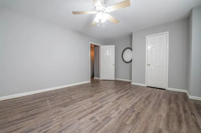 a view of an empty room with wooden floor and a ceiling fan